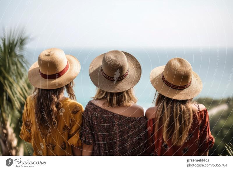Travel concept. Summer trip. Rear view of group of young diverse adult friends enjoying summer vacation day at sea. Women wearing straw hats looking at sea