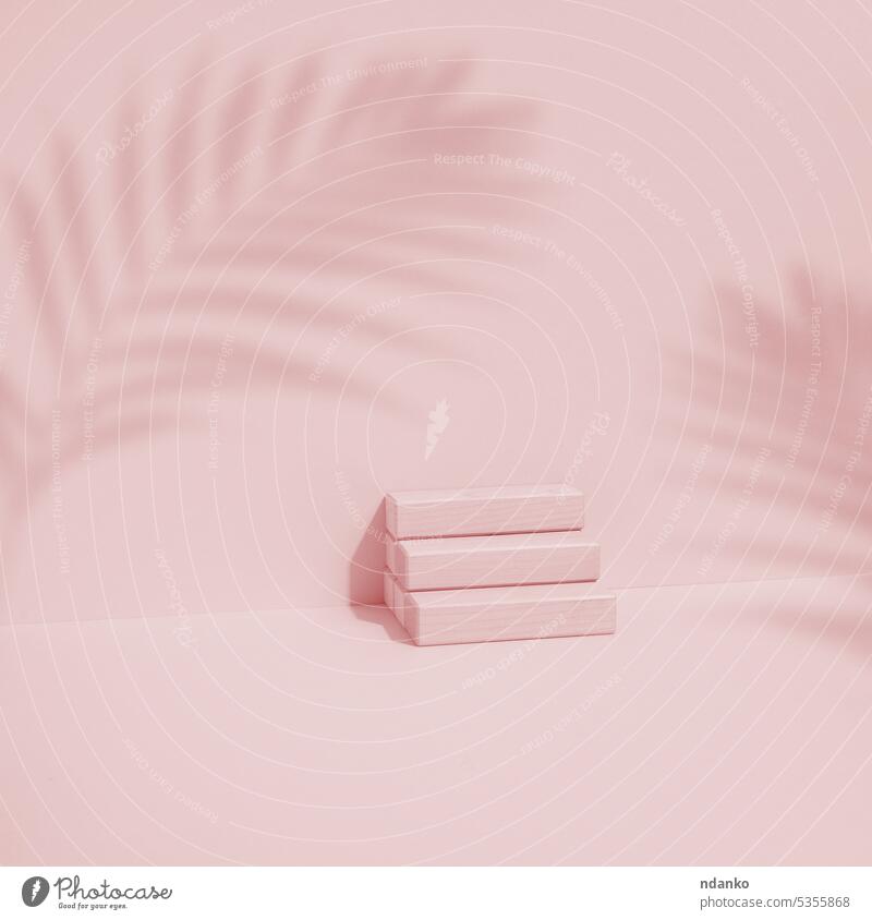 Wooden cube on a pink background with a shadow from a palm leaf. Stage for product demonstration, cosmetics. Promotion and advertising showcase stage stand