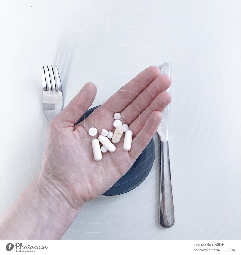A hand filled with tablets and capsules over a plate and cutlery Medication drugs medicine Illness Healthy Pill Health care Prescription Pharmacy