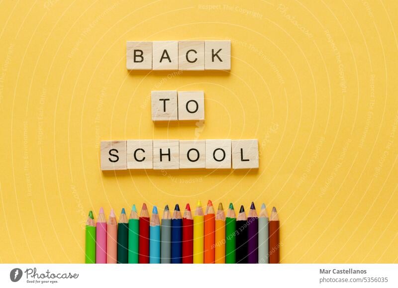 Back to class. Coloured pencils and letters BACK TO SCHOOL on yellow background. Copy space. Back to school cubes wood envelope Top view copy cream pastel black