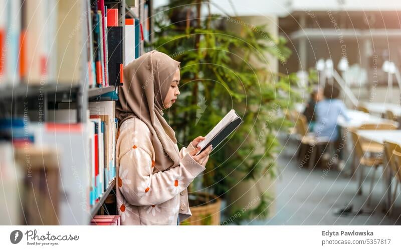 Young asian muslim woman reading book in a library real people teenager campus positive exam knowledge confident academic adult lifestyle academy adolescent