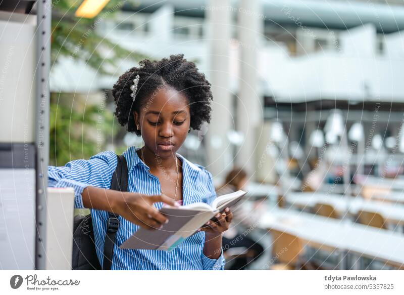 Black female student reading a book in a library real people teenager campus positive exam knowledge confident academic adult lifestyle academy adolescent