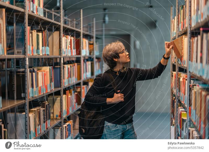 Portrait of asian student picking book from bookshelf in library real people teenager campus positive exam knowledge confident academic adult lifestyle academy