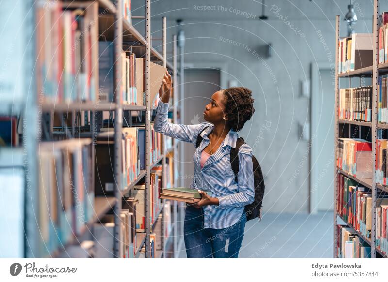 Black female student picking book from bookshelf in library real people teenager campus positive exam knowledge confident academic adult lifestyle academy