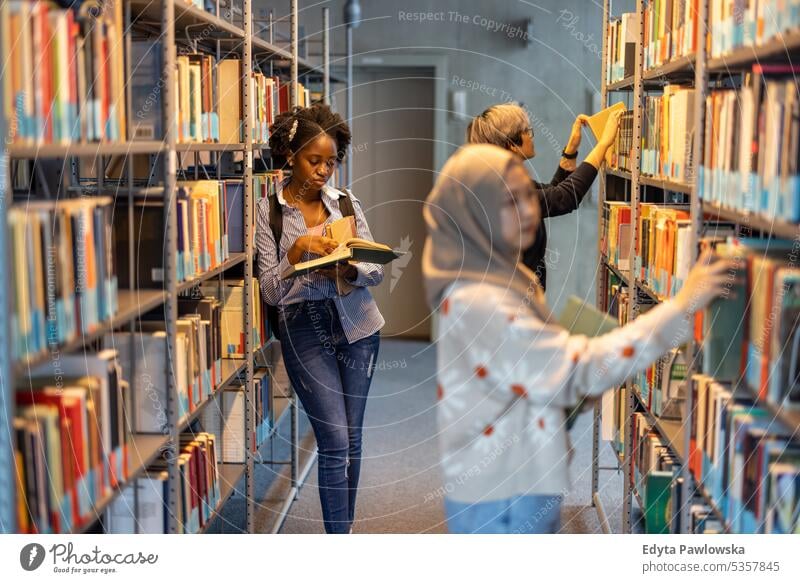Group of multiethnic students picking books from bookshelf in a library real people teenager campus positive exam knowledge confident academic adult lifestyle