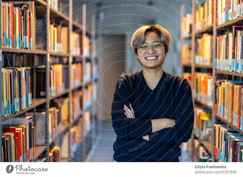 Portrait of smiling asian student standing with arms crossed in college library real people teenager campus positive exam knowledge confident academic adult