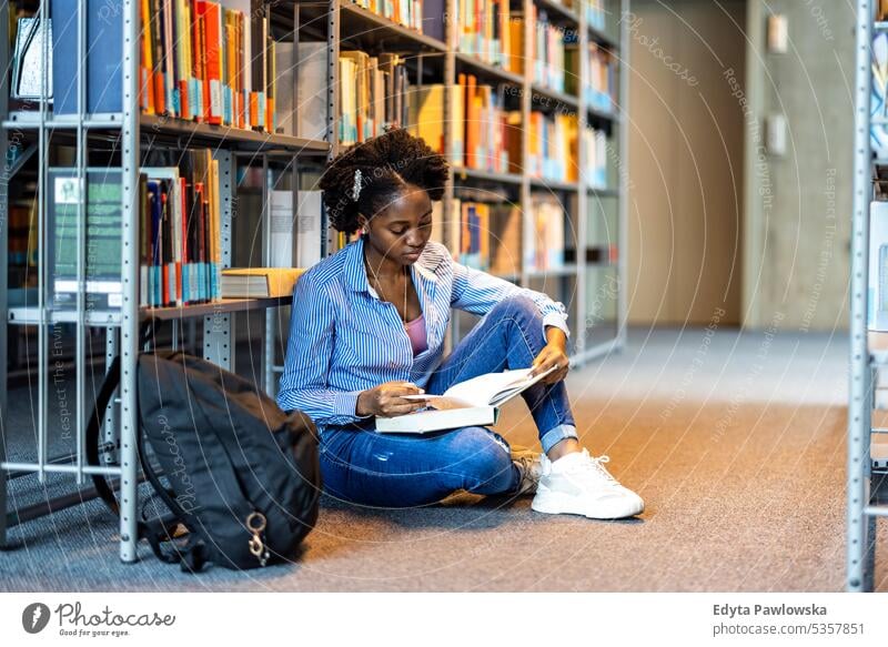 Black female student reading a book in a library real people teenager campus positive exam knowledge confident academic adult lifestyle academy adolescent