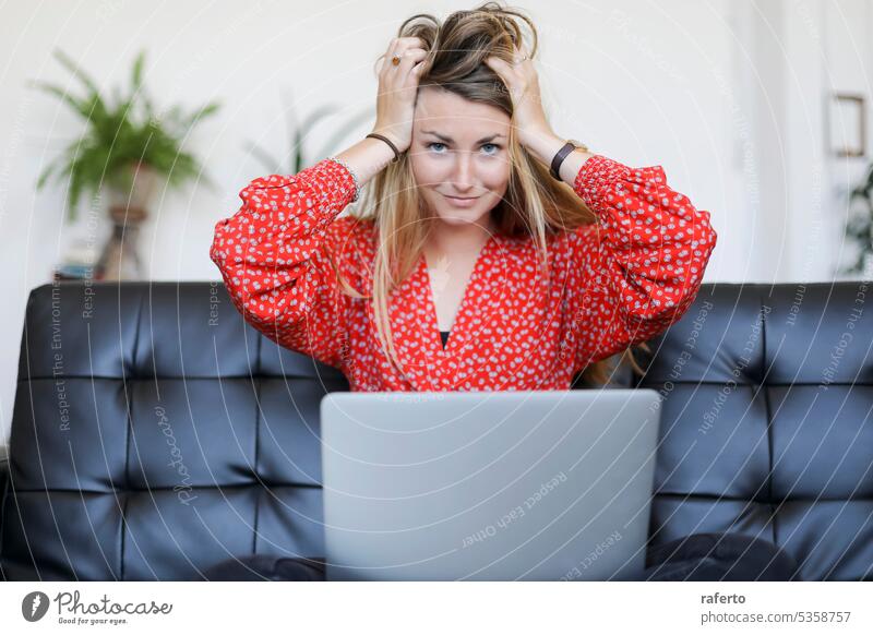 Blonde woman sitting on sofa and laptop with her hands on her head looking at the camera blonde hands on head looking at camera stress frustration tired