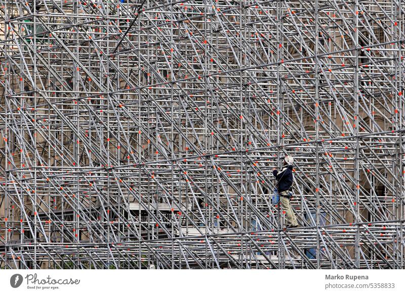 A worker on a scaffold working on a building scaffolding staging architecture construction development equipment frame growth helmet house incomplete industrial