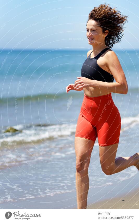 Smiling sportswoman running on sandy beach near seawater smile workout jog fitness barefoot summer young female happy energy activity seashore healthy lifestyle