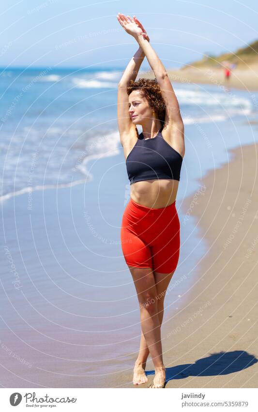 Fit woman stretching body on seashore sportswoman athlete training warm up beach exercise fitness workout ocean arms raised summer slim female young coast