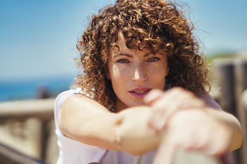 Young woman stretching arms on bridge pensive freckle curly hair portrait wavy hair calm casual fence brown hair posture alone lean brunette lonely human face