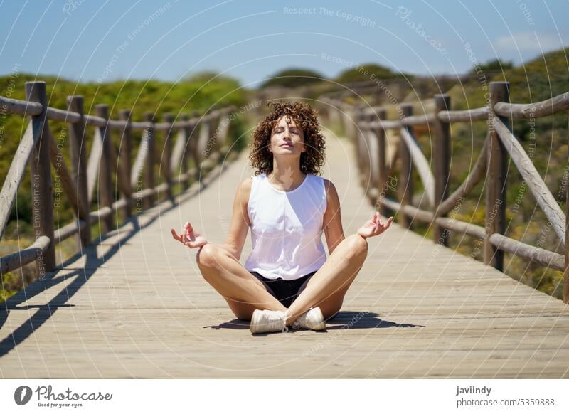 Relaxed young female meditating on wooden path meditate yoga practice woman lotus pose zen nature padmasana calm peaceful relax mindfulness wellness spirit