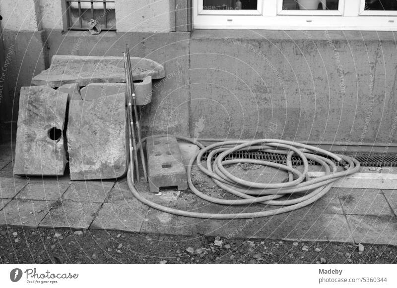 Garden hose next to old gray stones in a run-down backyard of gentrified Braubachstraße in the old town of Frankfurt am Main in Hesse in neo-realistic black and white