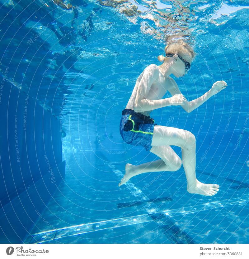 Blonde boy does a roll under blue water in swimming pool Boy (child) blonde hair blond boy Swimming pool underwater Underwater photo Coil warm warm weather