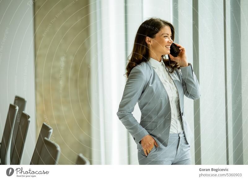Young woman using mobile phone by the office window adult alone attractive beautiful beauty bright brunette business business person businesspeople