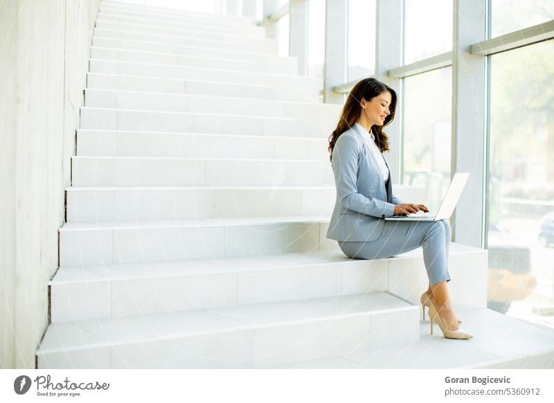 Young business woman sitting on the stairs on office hallway and working on laptop internet modern technology people happy beautiful communication female using