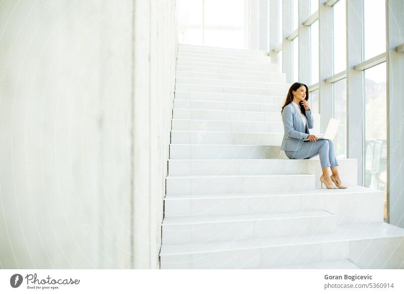 Young business woman sitting on the stairs on office hallway and working on laptop internet modern technology people happy beautiful communication female using