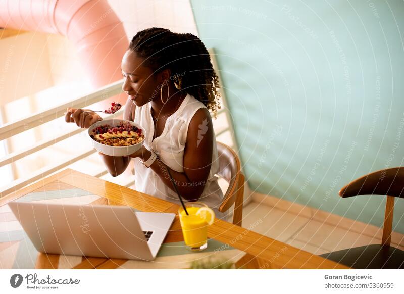 Young black woman having a healthy breakfast while working on laptop in the cafe african african american afro afro hairstyle attractive charming communication