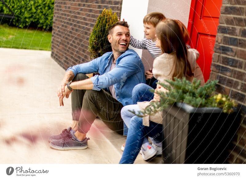 Family with a mother, father, son and daughter sitting outside on the steps of a front porch of a brick house parent stairs girl child kid happiness childhood