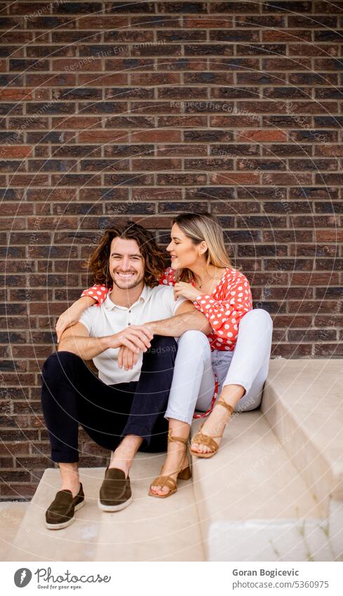 Smiling young couple in love sitting in front of house brick wall stairs outdoors woman caucasian facade cute two smile beautiful happiness casual female