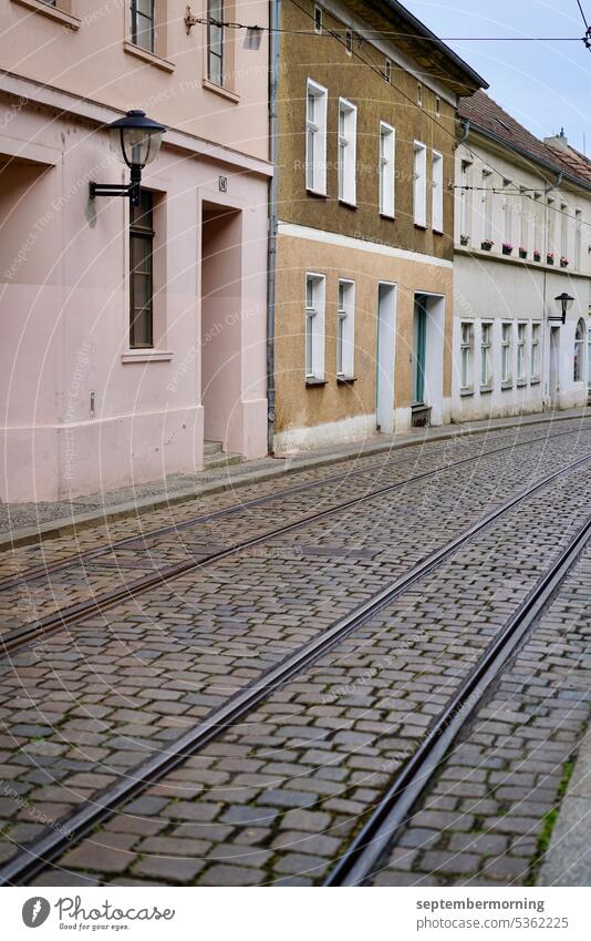 Cobblestone road with streetcar tracks Deserted old one-storey houses tram tracks pastel shades Cobblestones overcast sky