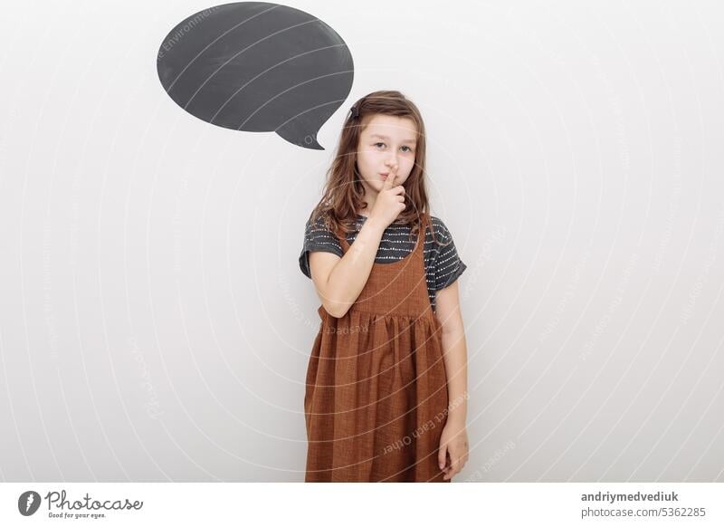 A little girl holds index finger near mouth, showing a gesture of silence. Isolated on white background. Shh. Secret. selective focus people pretty child