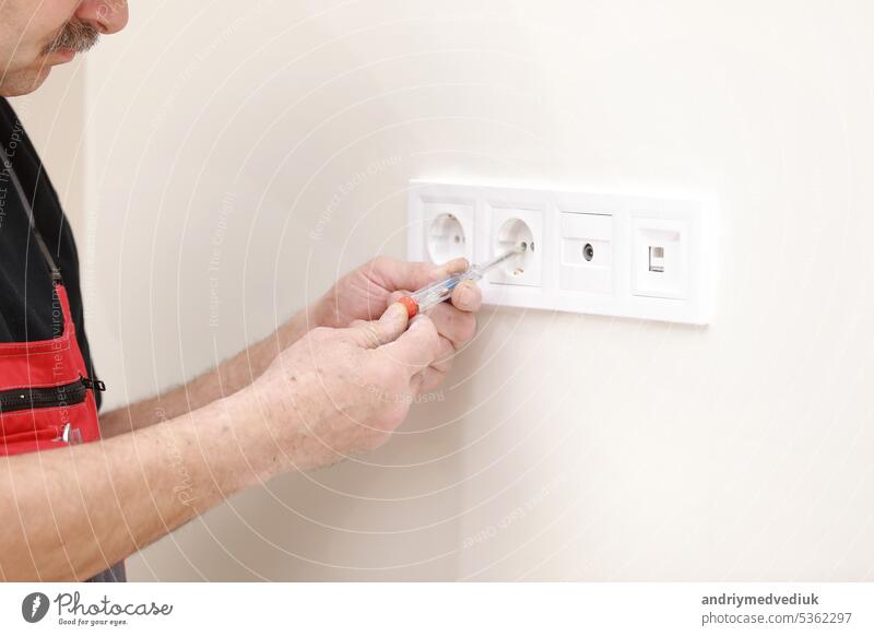Electrician hands tighten electrical wires in wall fixture or socket using a screw driver - closeup. Installing electrical outlet or socket - closeup on electrician hands