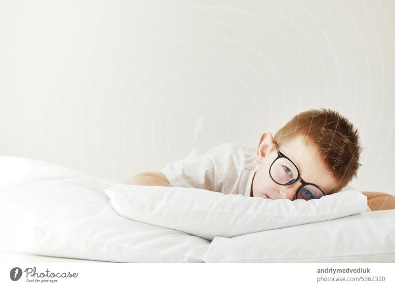 Adorable child boy in glasses is lying in bed. morning dreaming on white bed. baby sleeping pillow bedtime hand person kid face animal innocence little
