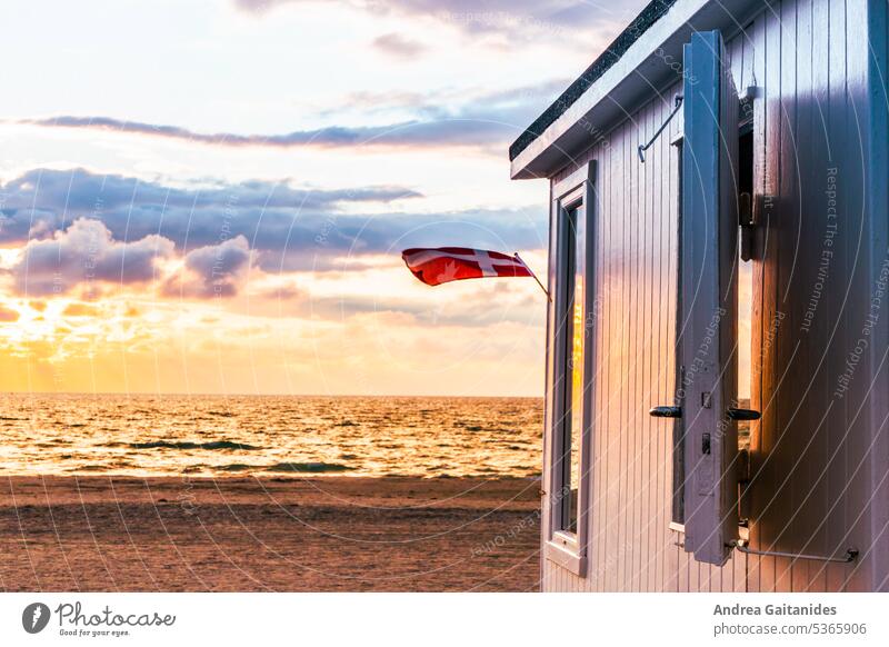 Partial view of bathhouse on Løkken beach during sunset, a Denmark flag waving in the wind, horizontal Bath house Changing cabine Danish Beach bay White Summer