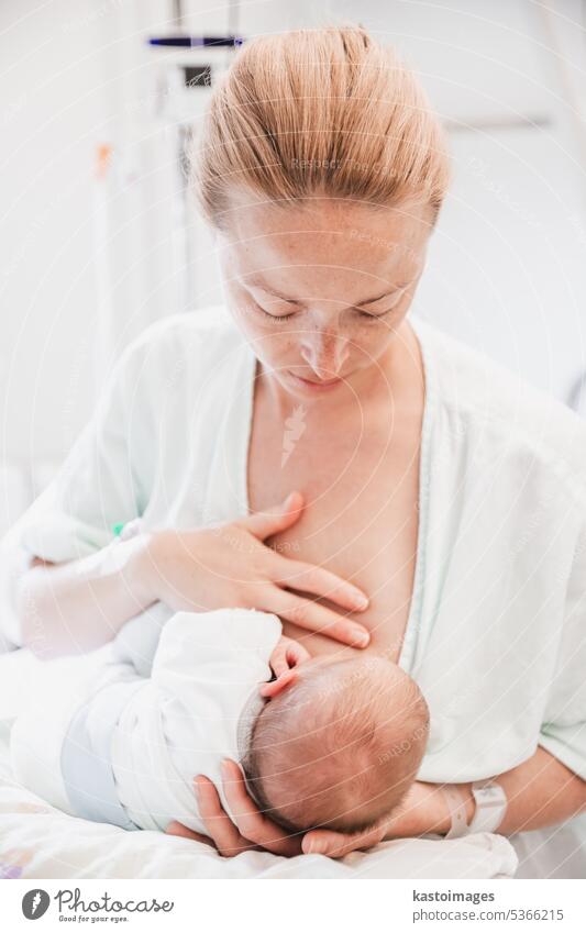 New mother carefully breastfeeds her newborn baby boy in hospital a day after labour. birth infant healthy young life pregnancy person motherhood mom giving two