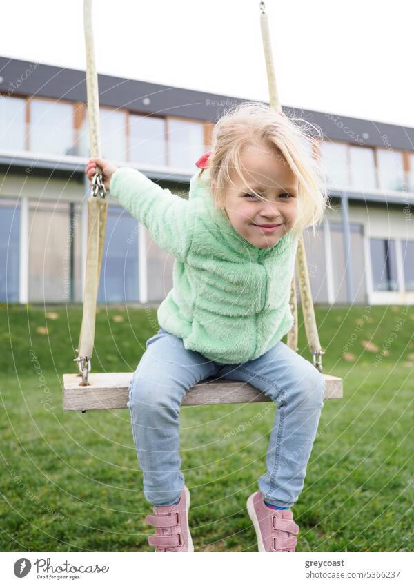 Little girl on a swing scandic active beautiful blonde cheerful childhood cute day enjoy entertainment female funny grass happiness having joyful knitwear