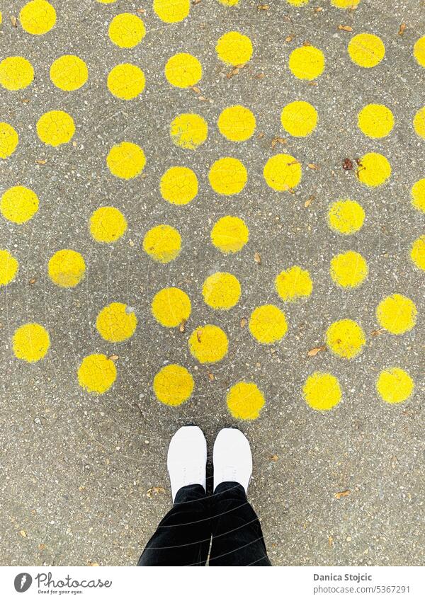 Yellow spotted road on the forecourt Abstract points yellow circles Street art Bird's-eye view Gray white sneakers black pants Concrete floor bright yellow