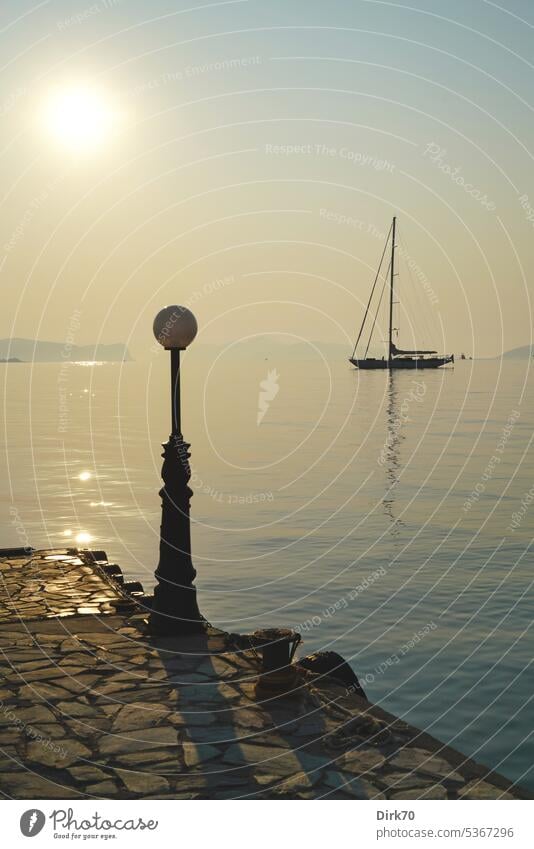 Sailboat at anchor in morning backlight with pier and lantern in foreground yacht sailing yacht Water Light Back-light Sun morning light Ocean the Aegean