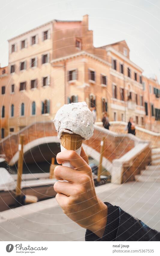 A scoop of stracciatella in a wafer - held in the foreground by a woman's hand. In the background something with Venice. Summer waffle ice Ice-cream cone