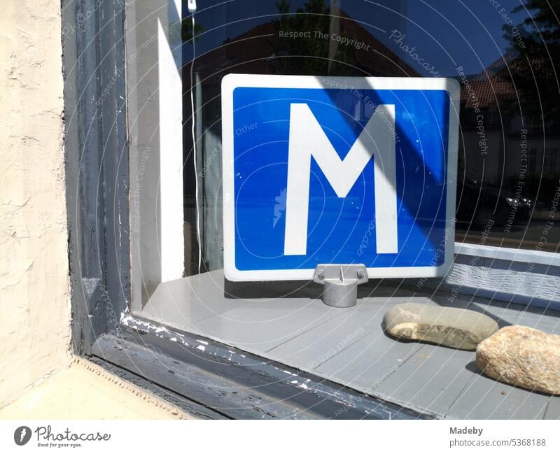White letter M on blue background on a sign in the shop window of a driving school in summer sunshine in Lemgo near Detmold in East Westphalia-Lippe, Germany