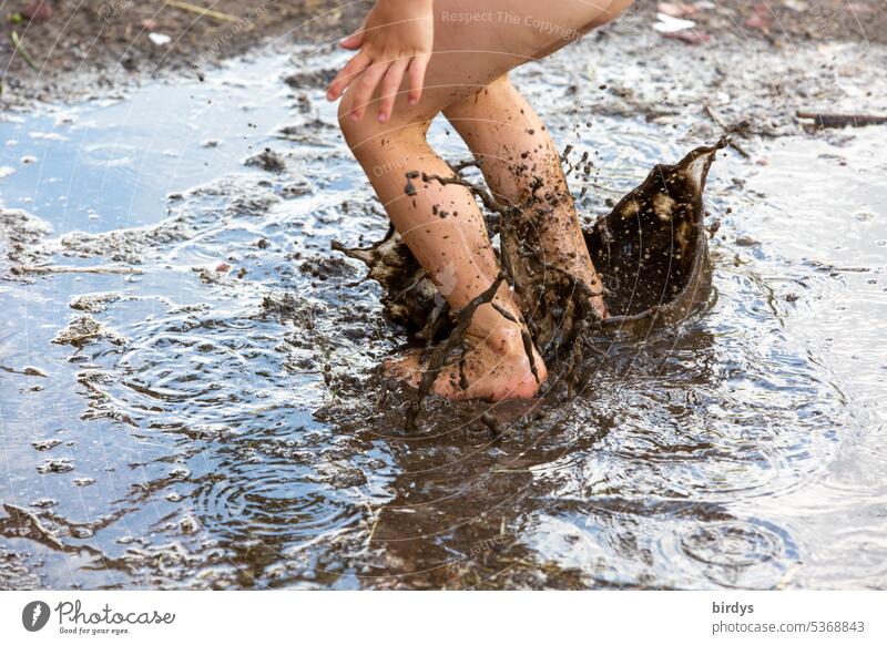 Child jumps into a puddle of mud slush Mud puddle Infancy Summer fun Puddle pawing around splash Jump Hop Playing active Happiness Legs Children's legs