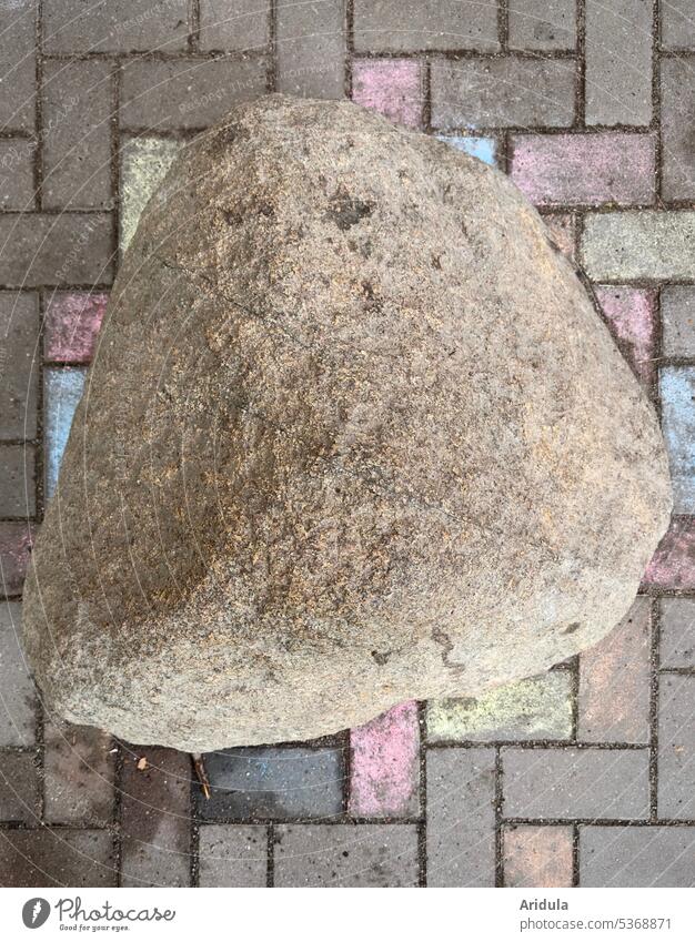 Large field stone on cobblestones partly painted with colorful chalk, bird's eye view Stone boulder foundling Paving stone Deserted Gray Lanes & trails