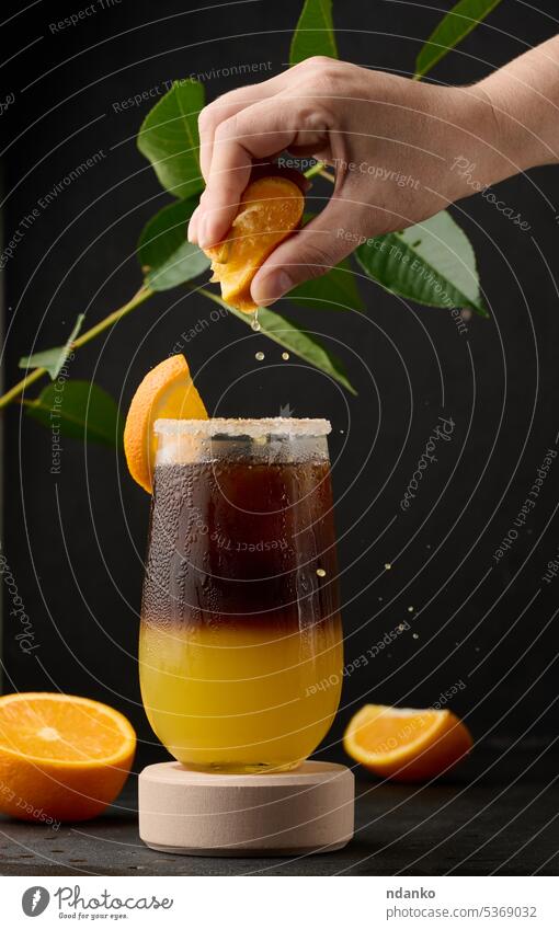 Iced coffee with orange juice in a transparent glass, a woman's hand squeezes an orange slice into a bubble drink layer brown sweet cool espresso cold fresh