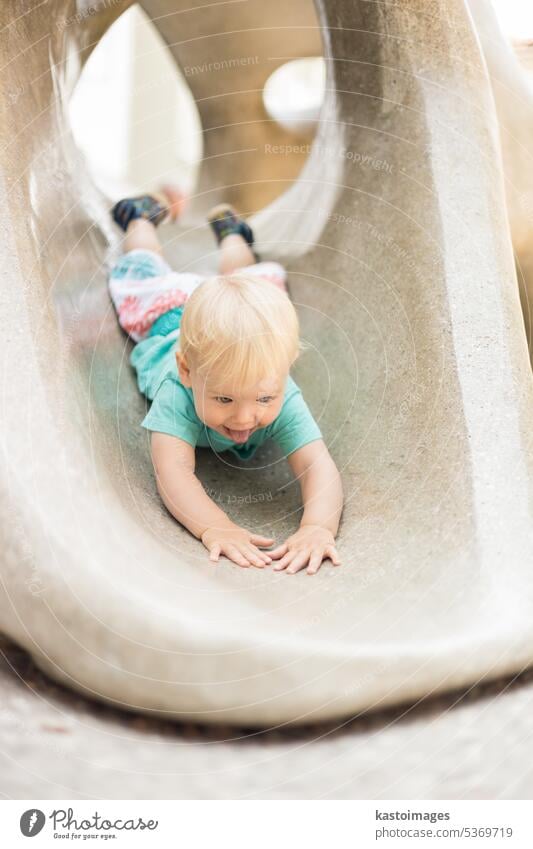 Child playing on outdoor playground. Toddler plays on school or kindergarten yard. Active kid on stone sculpured slide. Healthy summer activity for children. Little boy climbing outdoors.