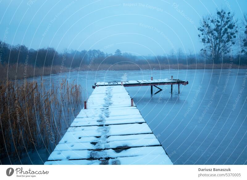 Snow on a wooden pier on the lake shore, view on a foggy December day snow water landscape nature blue outdoor weather calm sky bridge cold travel silence