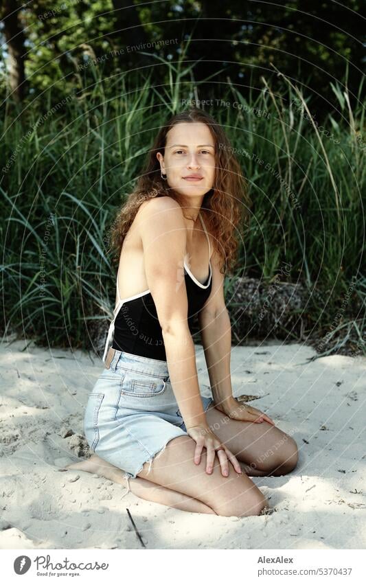 side portrait of young beautiful brunette woman kneeling in the sand in front of a forest warm Summery Beautiful weather plants proximity Day tranquillity