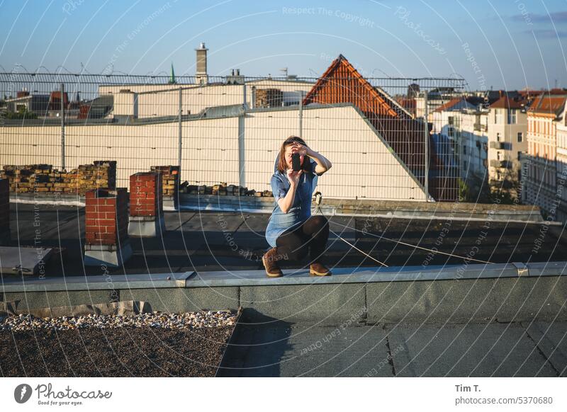 Young woman taking photos on the roof Woman Take a photo Berlin Prenzlauer Berg Town Exterior shot Capital city Downtown Colour photo Day Old town camera Roof