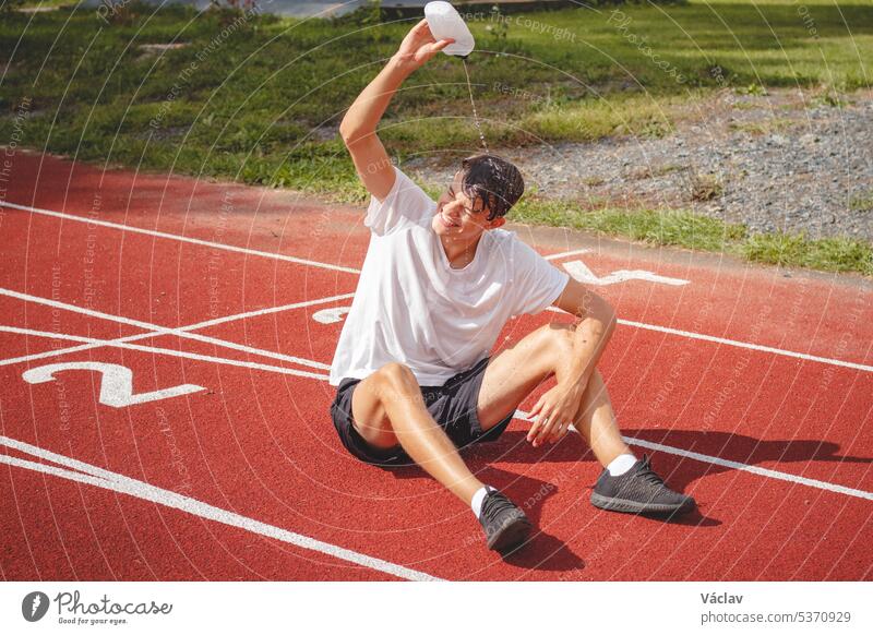 Young athlete refreshes himself with water after a hard workout on the athletic oval in the intense heat. Endurance training. Brown-haired adolescent person