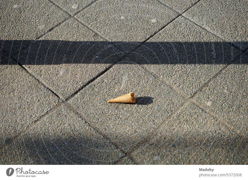 Remains of the wafer of an empty bitten ice cream cone on gray pavement in spring sunshine in the old town of Detmold in East Westphalia-Lippe, Germany