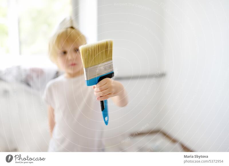 Little boy having fun with paint brush during repair of room. Do it yourself. child helper flat apartment walls renovation family design people paper home white