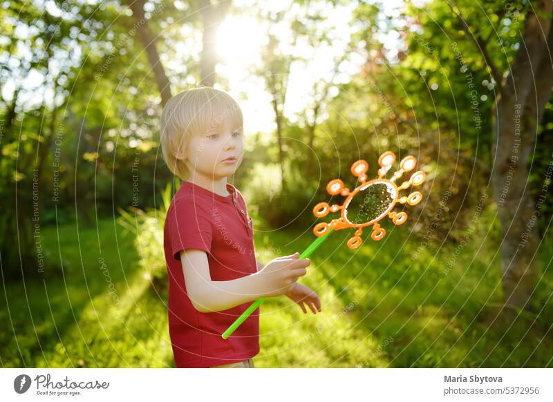Cute little boy is playing with big soap bubbles outdoor. Child is blowing big and small bubbles simultaneously. Summer leisure for kids. child fun outside
