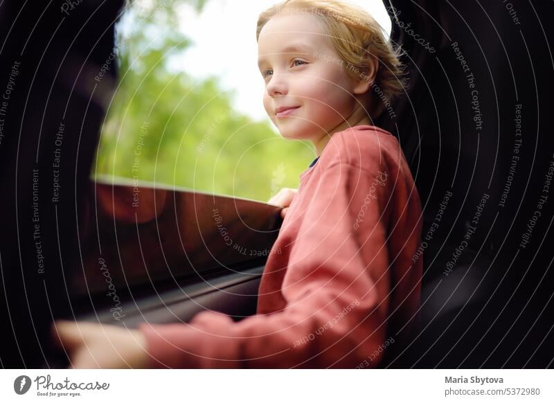 Cute preteen boy looking out through window of car during family road trip and enjoy of pleasant expectation of happy vacation. Joyful child travel with parents while holidays.