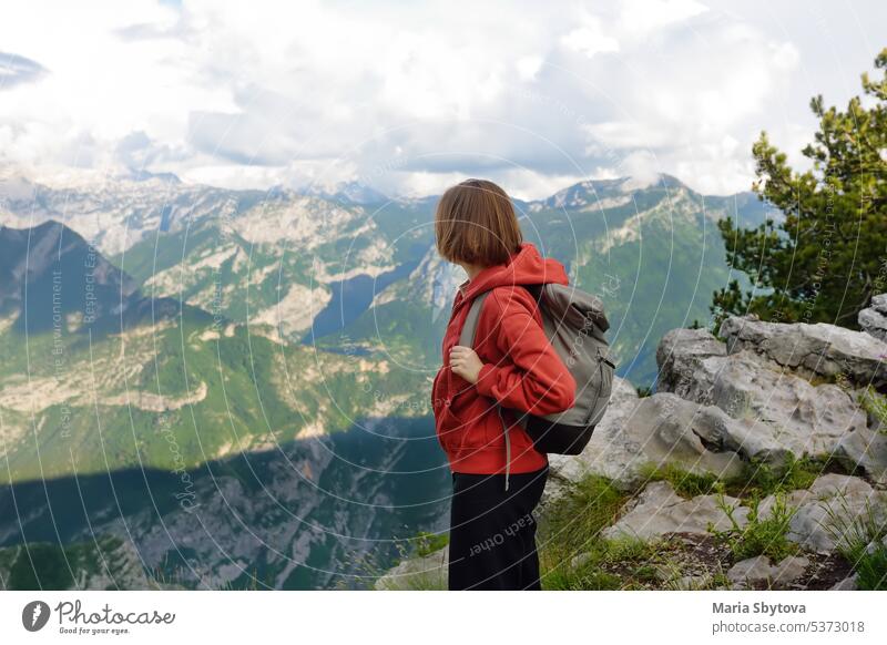 Side view of female hiker standing on stony slope of mountain valley during hiking trip. Young woman enjoying picturesque scenery with rocky peaks during trekking in Alps