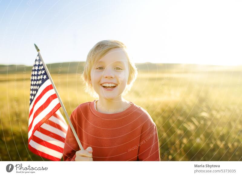 Cute little boy celebrating of July, 4 Independence Day of USA at sunny summer sunset. Child running with american flag of United States on wheat field. Proud small american boy holding country flag